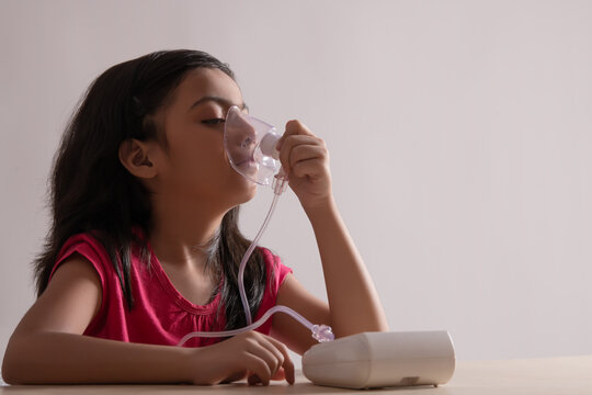 Young girl sitting and inhaling through a nebuliser at home. (Children) 