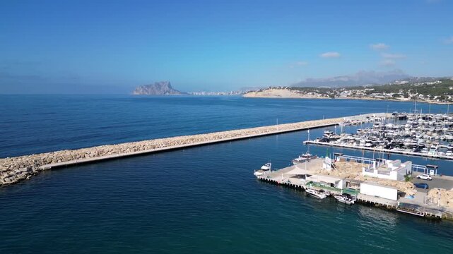 Aerial view of the marina in Moraira with numerous boats docked along the stone breakwater under a clear blue sky in Moraira, Valencian Community, Spain.