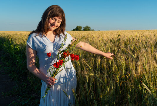 Young woman holding red poppies in a golden wheat field during sunset