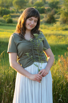 Young woman holding wild flowers in summer meadow at sunset