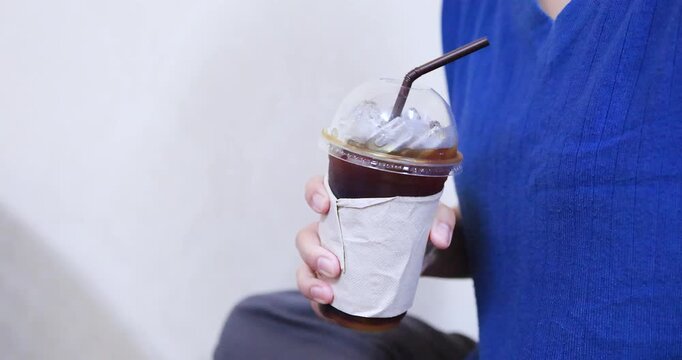 Hand holding an iced black coffee Americano in a plastic takeaway cup with ice. Ideal for cafe, beverage, refreshment, and lifestyle concepts