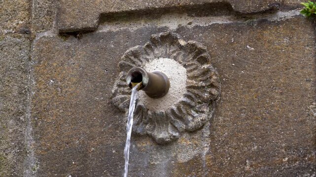 Detalle de la boca de una fuente antigua con el chorro de agua brotando, resaltando la textura de la piedra y el car&aacute;cter hist&oacute;rico del elemento.
