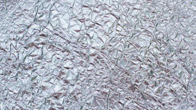 Crumpled Aluminum Foil Surface Shifts in a Seamless Stop Motion Loop, Creating a Clean Metallic Background for Typography and Design