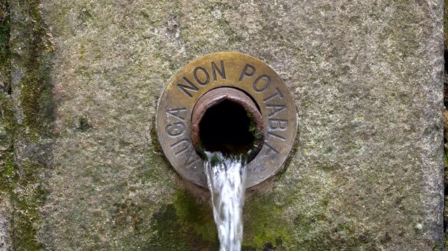 Detalle del ca&ntilde;o de una fuente de piedra con la inscripci&oacute;n &laquo;Auga non potable&raquo;, indicando que el agua no es apta para el consumo.