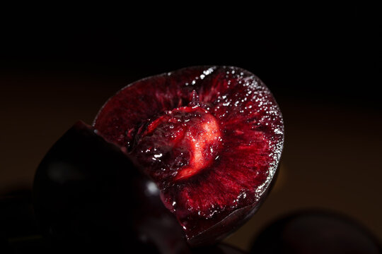 Close-up of sliced dark red cherry with glossy juicy flesh, visible pit cavity, rich texture, and dramatic low light macro detail against dark background for fresh food and dessert use