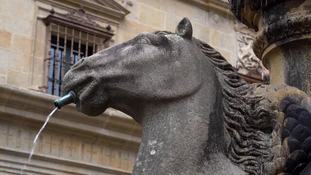 Detalle de la cabeza de un caballo convertida en fuente ornamental, con un chorro de agua saliendo por la boca de la escultura.