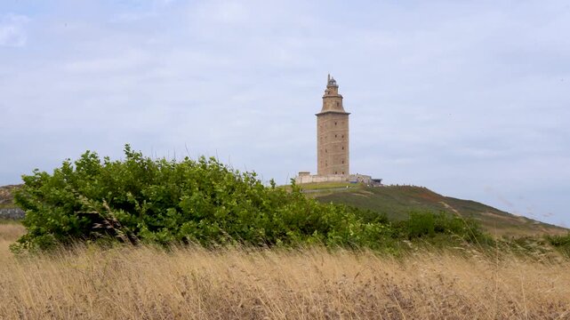 Vista panor&aacute;mica de la Torre de H&eacute;rcules en un d&iacute;a nublado, rodeada de praderas y paisaje campestre junto a la costa de A Coru&ntilde;a.