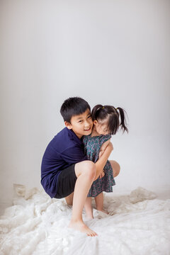 An Asian boy is holding a little girl and playing indoors.
