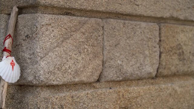 Detalle de un bord&oacute;n de peregrino con una vieira apoyado sobre una pared de piedra en la plaza del Obradoiro de Santiago de Compostela.