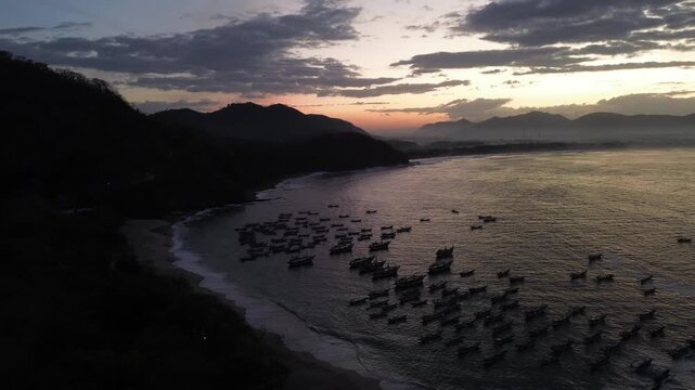 Aerial view of numerous traditional fishing boats anchored in the calm waters of Papuma Beach at sunset, East Java, Indonesia.
