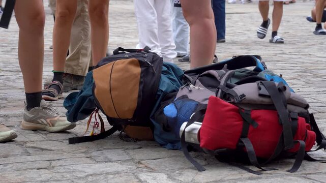 Mochilas descansando en el suelo de la plaza del Obradoiro, junto a las piernas de varios peregrinos tras su llegada a Santiago de Compostela.