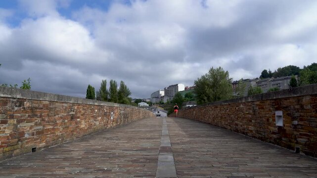 Vista desde el puente romano de Lugo con un deportista corriendo sobre su pavimento de piedra, junto al r&iacute;o Mi&ntilde;o y el paisaje natural.