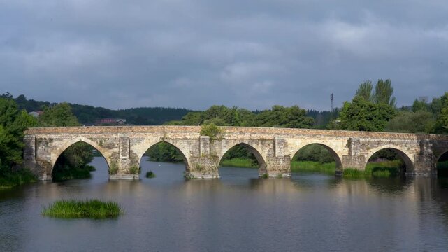 Vista general del puente romano de Lugo en un d&iacute;a nublado, sobre el r&iacute;o Mi&ntilde;o, mostrando su estructura hist&oacute;rica y el paisaje gallego.