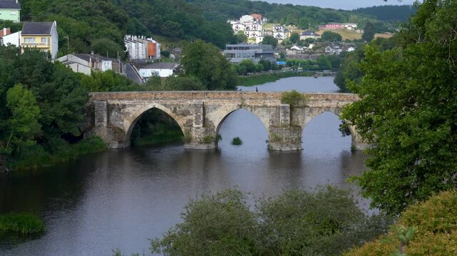Vista general del puente romano de Lugo en un d&iacute;a nublado, sobre el r&iacute;o Mi&ntilde;o, mostrando su estructura hist&oacute;rica y el paisaje gallego.