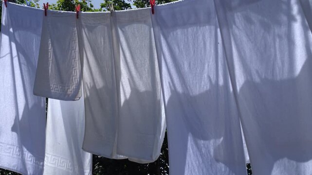 Detalle de s&aacute;banas y toallas blancas tendidas al sol con pinzas, movi&eacute;ndose suavemente por el viento en una escena dom&eacute;stica rural luminosa.
