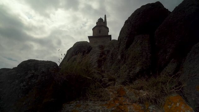 Plano picado de la Torre de H&eacute;rcules en un d&iacute;a nublado, mostrando el faro romano y el paisaje costero de A Coru&ntilde;a bajo un cielo cubierto.