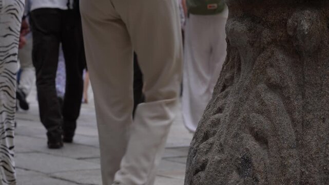 Detalle de las piernas de varios turistas entrando en la plaza del Obradoiro, en Santiago de Compostela, con el pavimento hist&oacute;rico en primer plano.