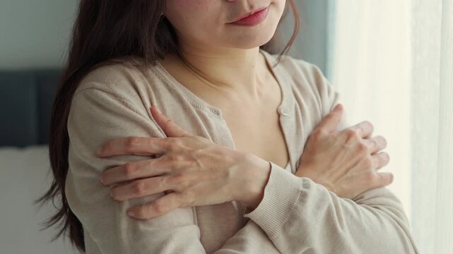 Cropped shot of a gentle woman hugging herself with a subtle smile and feeling safe, peaceful indoor lifestyle concept.