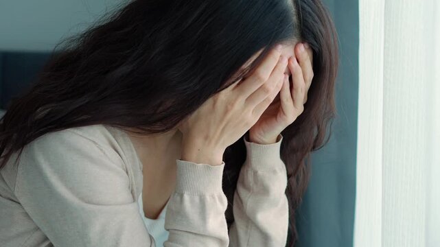 Depressed young Asian woman covering her face with hands in sadness and despair at home, Mental health problems and depression concept