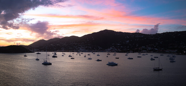 Aerial view of Charlotte Amalie bay at sunset with numerous boats anchored in calm water against rolling hills and a vibrant sky in Charlotte Amalie, St. Thomas, U.S. Virgin Islands.
