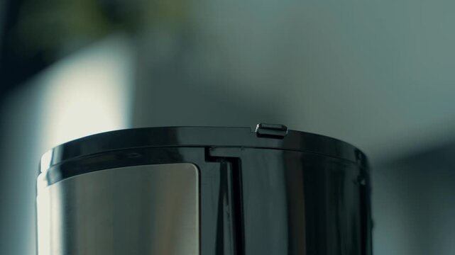 Closing the lid of the coffee maker. The hand closes the compartment in the coffee maker where the water is poured.