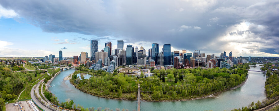 Aerial view of the Calgary skyline rising above the Bow River with lush green trees and dramatic storm clouds in the background in Calgary, Alberta, Canada.