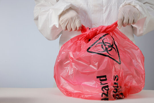 Cautious health worker wearing protective glove seals red biohazard waste storage bag with serious attention during clinical disposal process