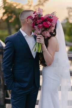 Newlywed couple hiding kiss behind pink wedding bouquet.