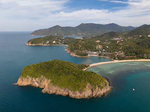 Aerial view of Ko Pha Ngan featuring lush green hills, a pristine sandy beach, and turquoise waters along the rocky coastline in Ko Pha-ngan District, Surat Thani, Thailand.