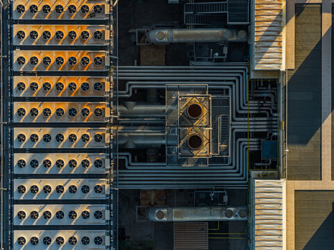 Aerial view of an industrial plant rooftop featuring rows of cooling fans and complex pipe systems under golden hour light in Rome, Lazio, Italy.