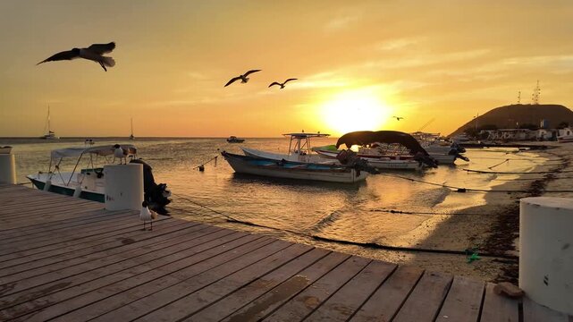 Serene evening landscape capturing the tranquil atmosphere of a tropical fishing pier as birds soar over moored boats under a glowing orange sky