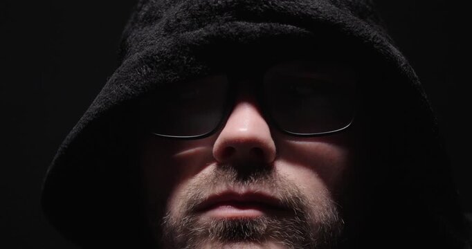 Close-up portrait of a hooded man in darkness, representing mystery, anonymity, secrecy, and cybercrime concepts.
