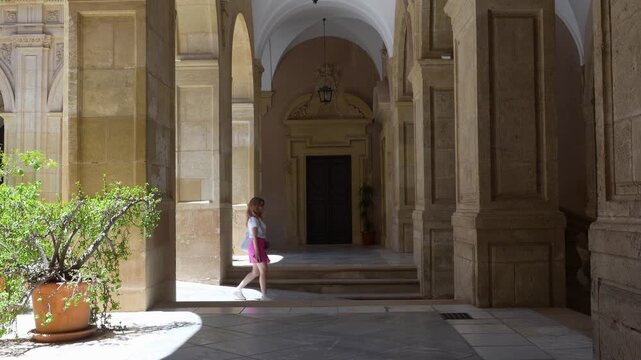 Girl walking in slow motion through a historic cloister with elegant stone arches in Murcia, Spain