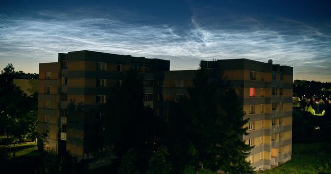 Rare noctilucent clouds glowing above silhouetted apartment buildings at twilight. Luminous night clouds create a striking atmospheric display over the urban skyline.