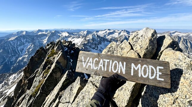 A hand holding a wooden signpost saying vacation mode at a snowy mountain peak summit.