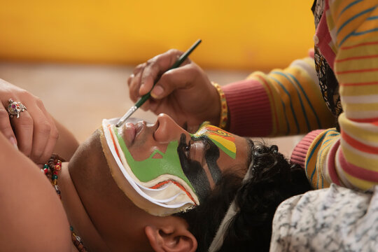 Kathakali dancer lying on the chatai and his makeup artist giving shape to the chutty on his face. 