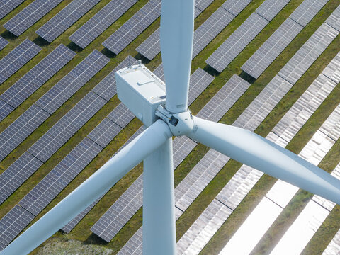 Aerial view of a large wind turbine standing in the middle of a vast solar farm with rows of photovoltaic panels in a green field, Poland.
