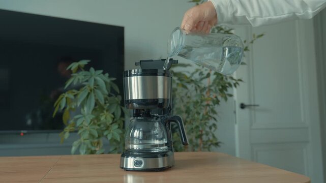 A man pours water from a pitcher into a coffee maker to make aromatic coffee at home. A weekend treat.
