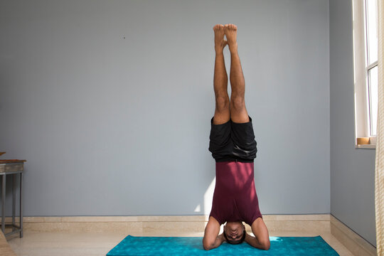 Man doing headstand on a yoga mat in his living room. 