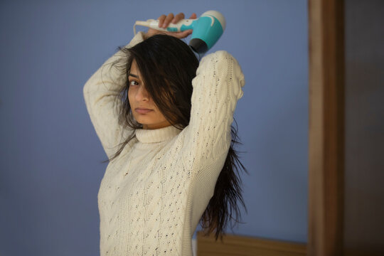 Woman drying her wet hair with a hairdryer in her bedroom. 