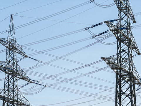 Aerial view of Amprion-Umspannwerk high-voltage transmission towers with intricate power lines against a clear blue sky in Pfungstadt, Hessen, Germany.