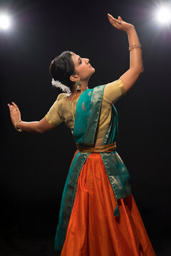 Kathak dancer giving a mesmerising performing in front of a dark background. 