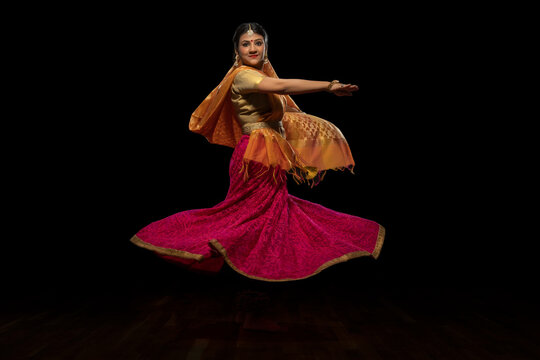 Kathak dancer circling gracefully during a performance in front of a dark background. 