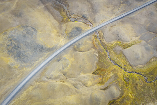 Aerial view of a road cutting through the barren volcanic landscape and mossy terrain of Iceland.