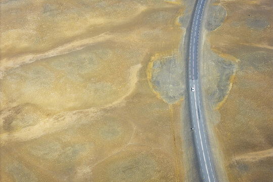 Aerial view of a lonely road winding through the vast, barren volcanic landscape with a single white car driving along the asphalt in Iceland.