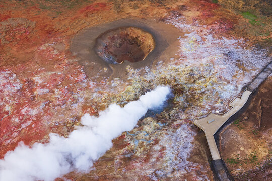 Aerial view of the Gunnuhver geothermal area with steam rising from vents, vibrant mineral-rich soil, and a wooden walkway in Grindavikurbaer, Iceland.