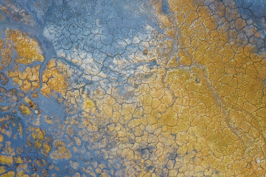 Aerial view of Hverir Sulfur Springs showing vibrant orange and blue mineral deposits and cracked earth patterns in Reykjahlid, Thingeyjarsveit, Iceland.