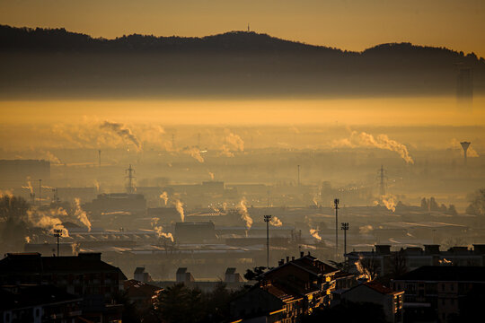 Aerial view of Turin covered in thick smog during golden hour with industrial chimneys emitting smoke over the cityscape in Turin, Piedmont, Italy.