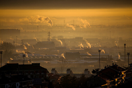 Aerial view of heavy smog and industrial smoke rising over the urban skyline of Turin during a golden sunset in Turin, Piedmont, Italy.