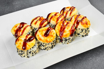 Baked sushi roll set with baked cheese topping and unagi sauce in takeaway box. Delicious Japanese rolls sprinkled with sesame seeds. Fresh gourmet Asian food. © Yaruniv-Studio
